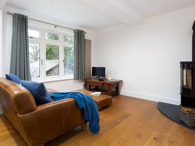 A living room with a brown leather sofa blue cushions and throw a wooden table with a small tv and a wood stove with a basket of logs at Wynford Ambleside