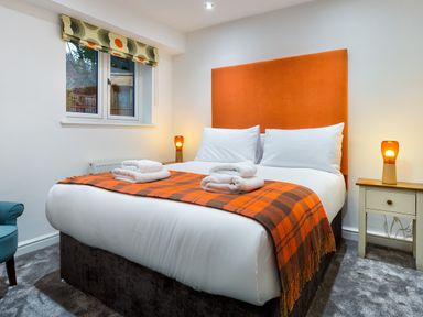 A bedroom with a bed with an orange headboard and a plaid throw with towels on it at Wynford in Ambleside