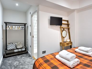 A bedroom with an orange plaid bedspread and folded towels a wooden shelf with a mirror a black clothing rack with hangers and baskets at Wynford in Ambleside