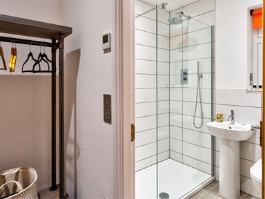 A bathroom with a glass-enclosed shower and a sink next to a closet with hangers and a laundry basket at Wynford in Ambleside