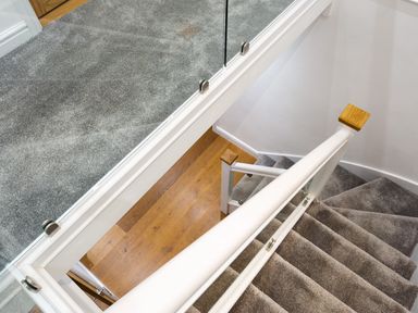 A staircase with grey carpet and a glass railing overlooking a wooden floor at Wynford in Ambleside