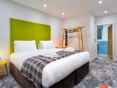 A bedroom with a large bed with white sheets and green headboard and an open door leading to a bathroom at Wynford in Ambleside