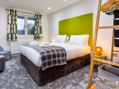 A bedroom with a double bed with a green headboard and towels on top at Wynford in Ambleside