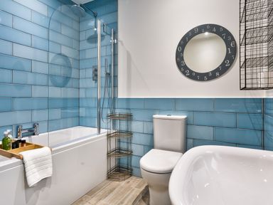 A bathroom with blue tiled walls a bathtub a toilet a mirror and a metal shelf at Wynford in Ambleside