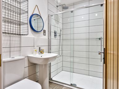 A bathroom with a toilet sink round mirror and glass shower enclosure at Wynford in Ambleside