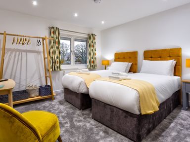 A bedroom with two single beds with yellow headboards and throws a yellow chair and a wooden clothes rack at Wynford in Ambleside