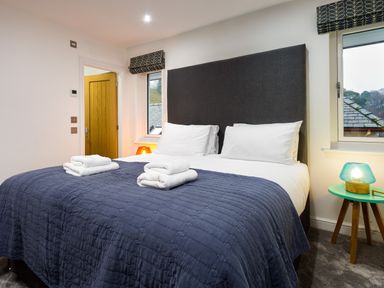 A bedroom with a large bed covered with a blue quilt and white towels on top with bedside tables and windows at Wynford in Ambleside