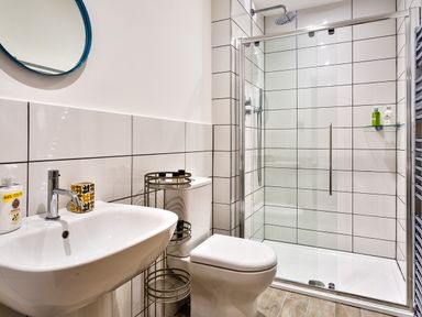 A bathroom with a white sink and toilet next to a glass shower enclosure with tiled walls at Wynford in Ambleside