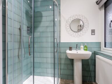 A bathroom with a glass shower enclosure and a white pedestal sink with a round decorative mirror above at Wynford in Ambleside
