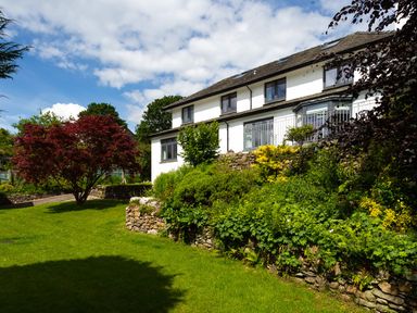 A garden with lawn trees and stone walls outside a white house at Wynford in Ambleside