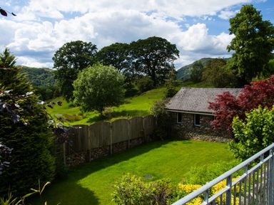 A fenced garden with green grass and trees near a stone building at Wynford in Ambleside