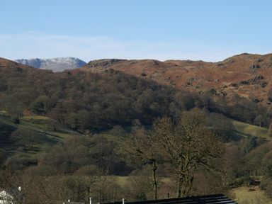 A view of hills and bare trees with snow on distant mountains at Wynford in Ambleside