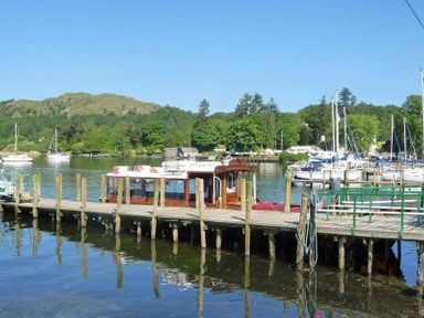 A wooden dock with a boat moored on a lake with hills and trees in the background at Wynford in Ambleside
