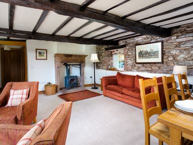 A living room with armchairs a sofa a wood burning stove wooden dining chairs and a table at Horrockwood Farm in Watermillock