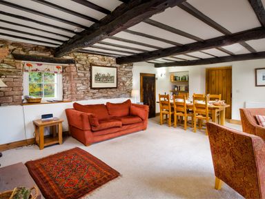A living room with a red sofa wooden dining table with chairs and exposed wooden beams at Horrockwood Farm in Watermillock