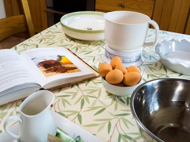 A kitchen table with eggs bowls a jug a kitchen scale and a cookbook at Horrockwood Farm in Watermillock