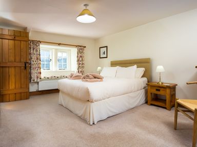 A bedroom with a bed bedside table lamp wooden door and window with floral curtains at Horrockwood Farm in Watermillock