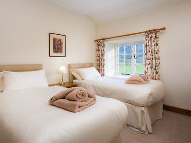 A bedroom with two single beds white bedding bedside table lamp window with floral curtains at Horrockwood Farm in Watermillock