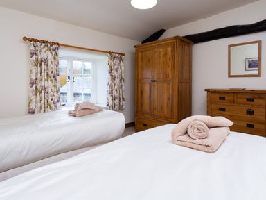 A bedroom with two single beds with towels on them wooden wardrobe wooden dresser and a window with floral curtains at Horrockwood Farm in Watermillock