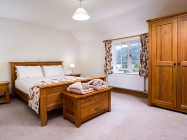 A bedroom with a wooden bed and wardrobe next to a window with floral curtains at Horrockwood Farm in Watermillock
