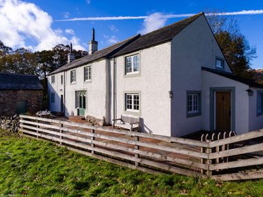 A white house with green window frames and a wooden fence in front at Horrockwood Farm in Watermillock