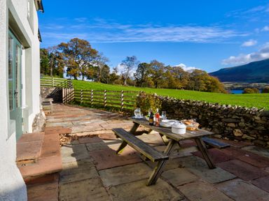 A patio with a wooden picnic table set with dishes and bottles overlooking a green field and stone wall at Horrockwood Farm in Watermillock