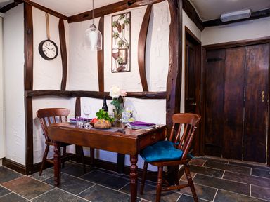 A dining area with a wooden table and two chairs set with plates glasses and cutlery at Tipsy Gin Cottage Crosthwaite