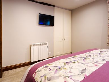 A bedroom with a mounted TV radiator and wardrobe at Tipsy Gin Cottage in Crosthwaite