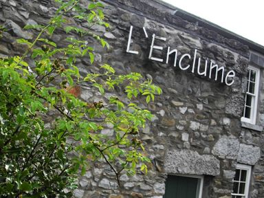 A stone building with the sign L Enclume and a green door partially visible with greenery in the foreground at Tipsy Gin Cottage in Crosthwaite