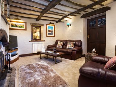 A living room with brown leather sofas a coffee table a TV and a fireplace at Tipsy Gin Cottage Crosthwaite