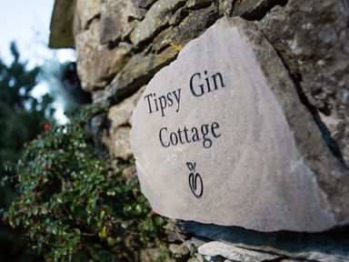 A stone plaque engraved with Tipsy Gin Cottage mounted on a stone wall with greenery nearby at Tipsy Gin Cottage in Crosthwaite