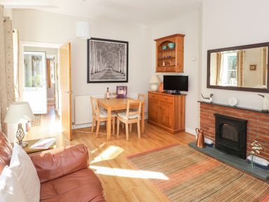 A living room with a brown leather sofa wooden dining table wooden cabinet and a brick fireplace at Courtyard Cottage Ambleside