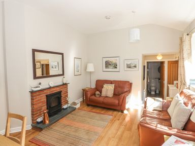 A living room with two brown leather sofas a brick fireplace with a mirror above and a view into a bathroom at Courtyard Cottage in Ambleside