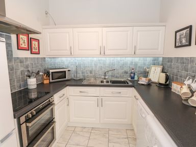 A kitchen with white cabinets grey tiled backsplash black countertops a double oven microwave sink and various kitchen utensils at Courtyard Cottage in Ambleside