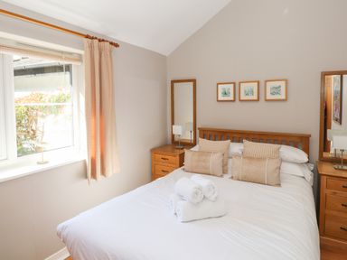 A bedroom with a double bed white bedding beige pillows wooden bedside tables and mirrors at Courtyard Cottage in Ambleside