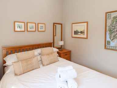 A bedroom with a wooden bed frame white bedding pillows rolled towels bedside table lamp mirror and framed pictures on the walls at Courtyard Cottage in Ambleside