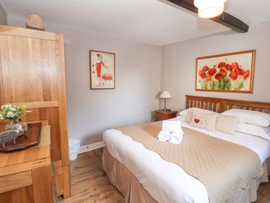 A bedroom with a wooden bed and nightstand a wardrobe and two framed pictures at Courtyard Cottage in Ambleside