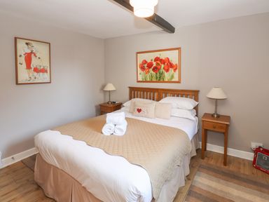 A bedroom with a double bed between two wooden nightstands with lamps and paintings on the walls at Courtyard Cottage in Ambleside