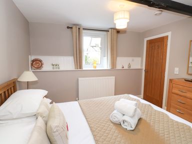 A bedroom with a bed with folded towels on it next to a window with curtains and a wooden dresser at Courtyard Cottage in Ambleside