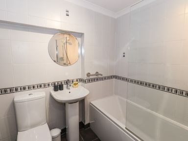 A bathroom with a toilet sink round mirror and bathtub with shower at Courtyard Cottage in Ambleside