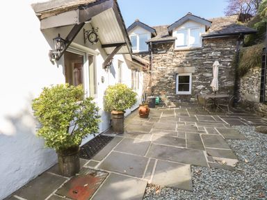 A stone patio with potted plants a table and chairs outside a stone and white cottage at Courtyard Cottage in Ambleside