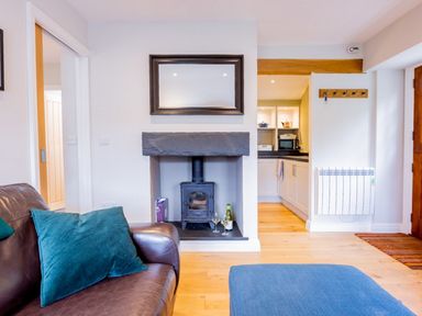A living room with a brown leather sofa with teal pillows a wood burning stove under a mirror and a blue ottoman at Barn End in Ambleside