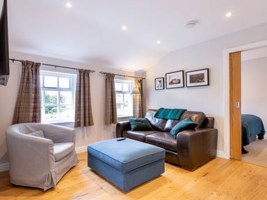 A living room with a brown leather sofa green cushions blue ottoman gray armchair and three framed pictures on the wall at Barn End in Ambleside