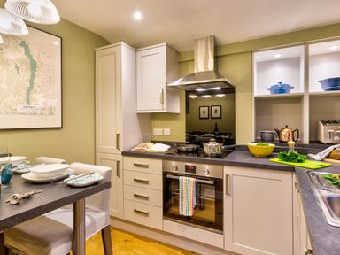 A kitchen with white cabinets a black countertop and a dining table set at Barn End Ambleside