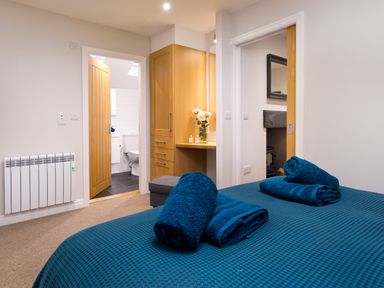 A bedroom with a blue bedspread and rolled towels with doors leading to a bathroom and another room at Barn End Ambleside