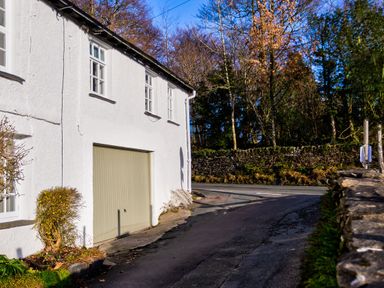 A white building with three windows and a closed garage door next to a road and trees at Barn End in Ambleside