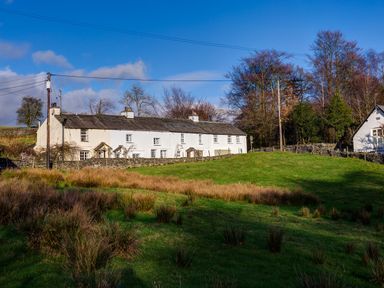 A row of white terraced cottages behind a stone wall with grass and trees at Barn End in Ambleside