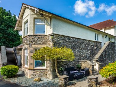 An exterior view of a two story stone and plaster house with outdoor seating and stairs at Skyfall in Bowness