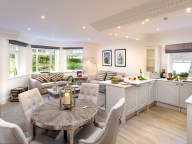 An open plan kitchen and living room with a round dining table four chairs two sofas and white kitchen cabinets at Skyfall in Bowness