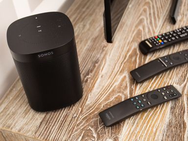 A black Sonos speaker and three remote controls on a wooden table at Skyfall in Bowness